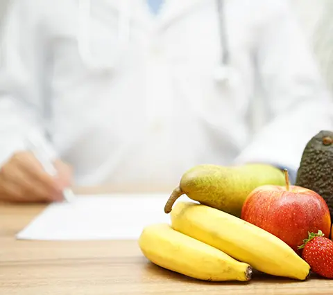 frutas frescas sobre escritorio con médico gastroenterólogo escribiendo al fondo