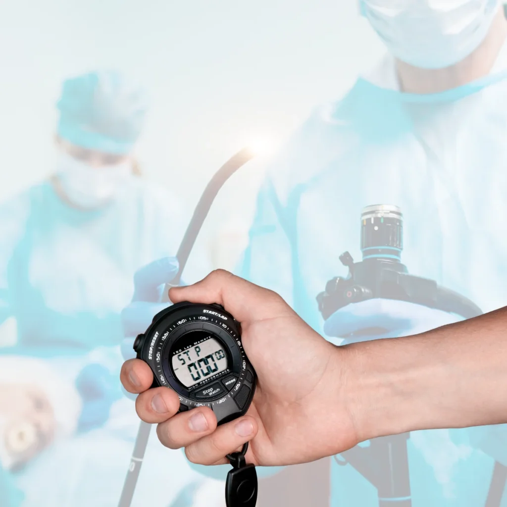 médico en el fondo realizando una endoscopia, desde la parte lateral una mano con un cronómetro para dar significado de cuanto dura una endoscopia